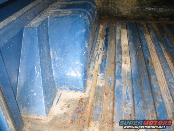 Interior of a blue truck bed with ribbed floor and some rust