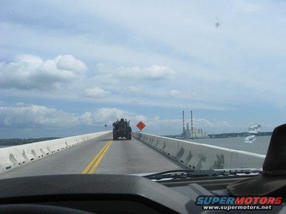 Heavy-duty truck driving on a bridge with a power plant in the background