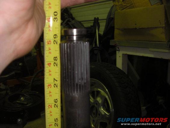 Measuring tape next to a splined shaft, with a tire and wheel in the background