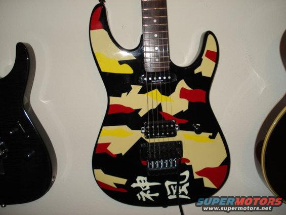 Electric guitar with camouflage paint and Japanese characters, next to a black guitar