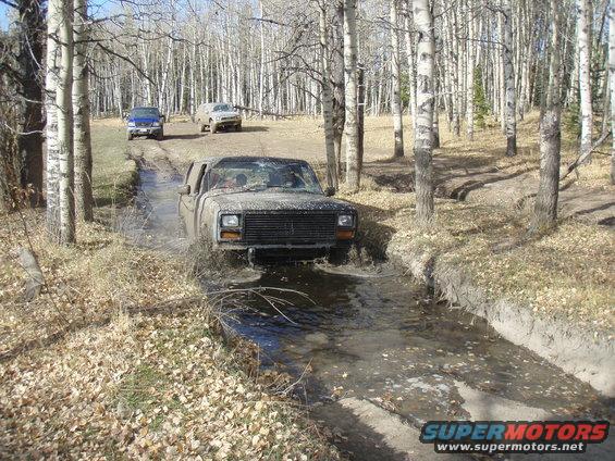 Muddy pickup truck driving through water with other vehicles behind it