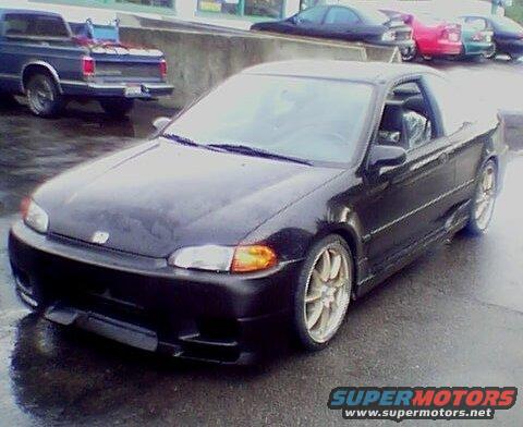 Black coupe with aftermarket body kit and gold wheels parked on wet asphalt
