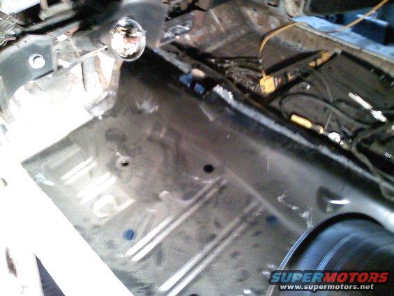 Car interior floor pan with exposed metal and wiring, viewed from above