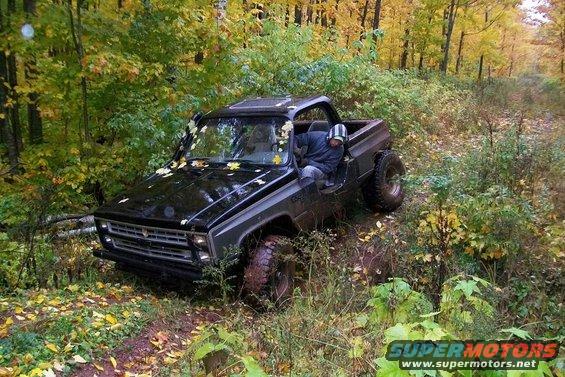 1988 Chevrolet Blazer with lifted suspension and off-road tires driving on a wooded trail
