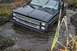 1988 Chevrolet Blazer - A black pickup truck is stuck in a muddy, water-filled ditch with tall grass on the sides.