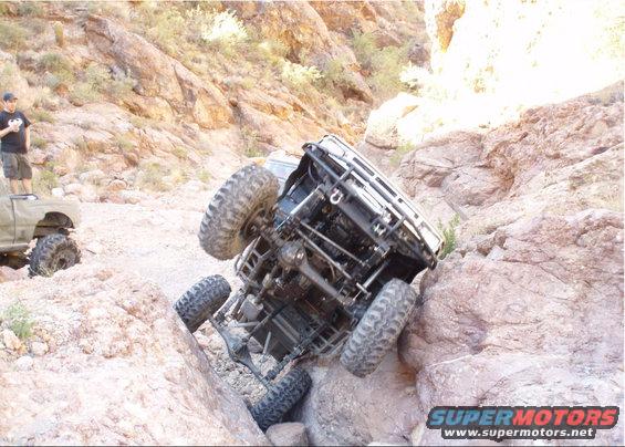 Off-road vehicle tipped over on rocky terrain with another truck nearby