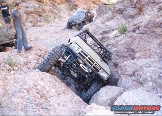 Tan off-road pickup truck with a roll cage navigating a rocky canyon, front 3/4 view