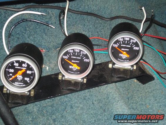 Three aftermarket gauges (oil pressure, water temp, trans temp) mounted on a black bracket with wiring