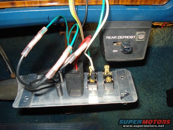 Close-up of aftermarket wiring and switches mounted on a metal plate, with a rear defrost switch visible