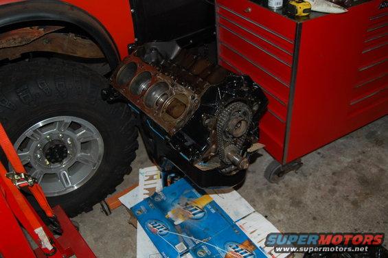 Engine block with timing chain and gears next to a large tire and a red toolbox