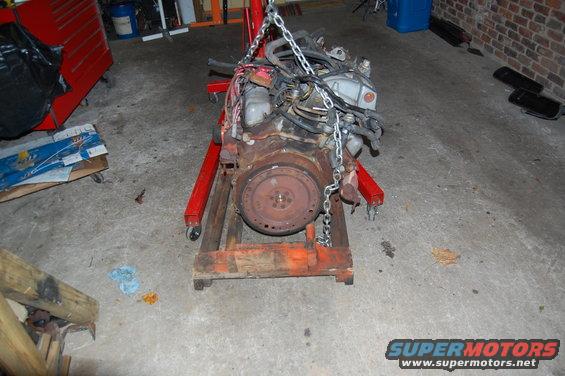 Engine assembly suspended by chains on a red engine stand in a garage