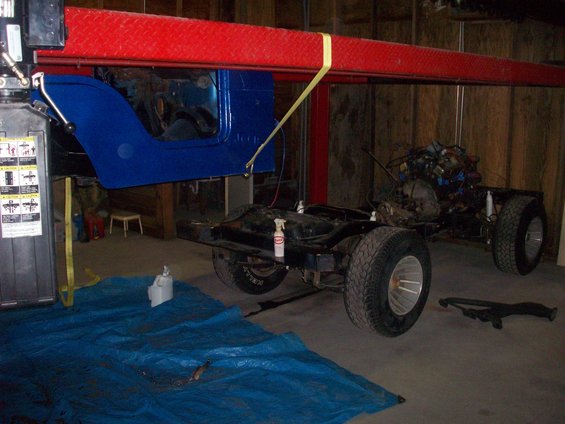 Blue Jeep CJ body lifted above chassis with engine and drivetrain visible