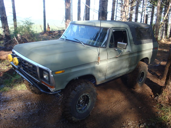 Olive green 1978 Ford Bronco on a dirt trail with yellow fog lights