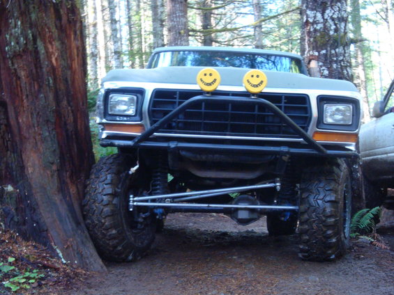 1978 Ford Bronco with custom bumper and smiley face lights, parked in a forest