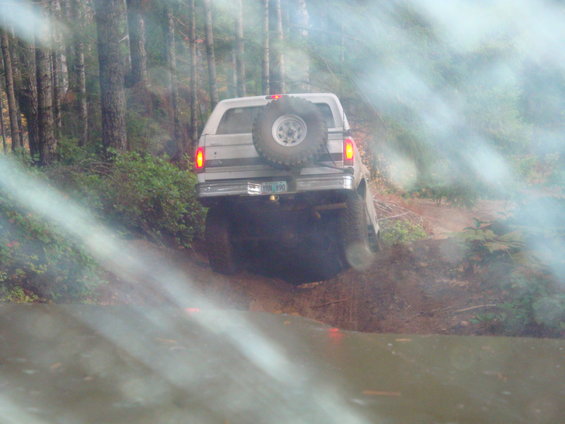 Silver Ford Bronco climbing muddy hill, spare tire on back