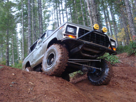 1978 Ford Bronco with custom bumper and off-road tires climbing a dirt hill in a forest