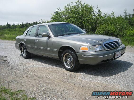 Gray sedan parked on gravel, front quarter view. Chrome grille, amber turn signals, license plate visible
