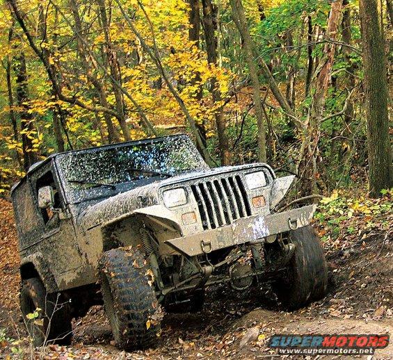 Mud-covered 1991 Jeep Wrangler driving on a dirt trail in a forest with yellow autumn leaves