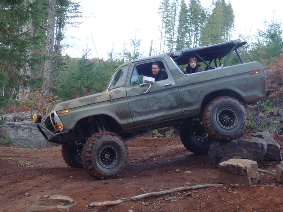 Olive green 1978 Ford Bronco with lifted suspension and large tires climbing over rocks on a dirt trail