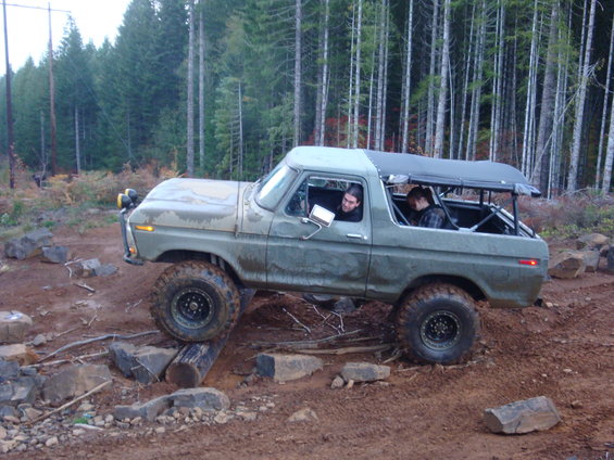 Green 1978 Ford Bronco off-roading over logs