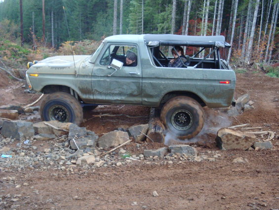 1978 Ford Bronco driving over rocks on a dirt trail, with two people inside