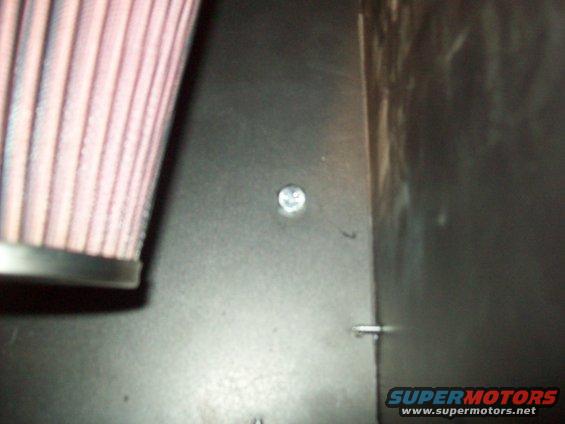 Close-up of a pink and white striped air filter next to a dark metal panel with a silver screw