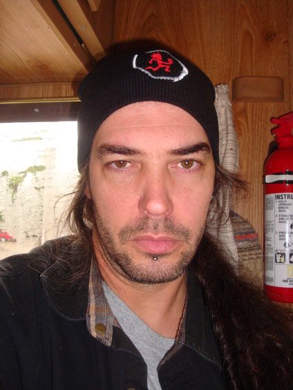 Man wearing a black beanie with a red running man logo, inside a vehicle. Fire extinguisher visible