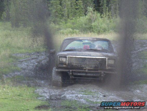 Ford Bronco driving through mud, kicking up spray. Front view