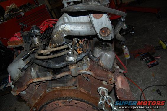Engine block with fuel lines, distributor, and intake manifold. Rusty components visible