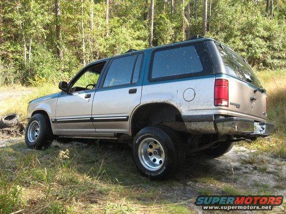 Silver and teal 1992 Ford Explorer parked on a dirt path with trees in the background