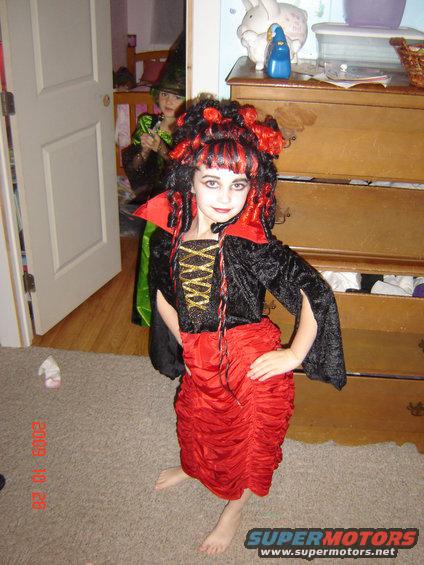 Children in Halloween costumes stand in a room with a dresser and a door