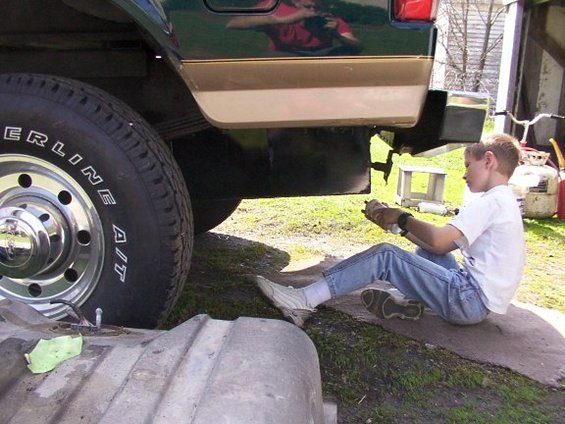 Green and tan truck chassis with a boy working on a fuel tank, side view