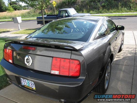 Dark gray Ford Mustang coupe parked on driveway, with a blue pickup truck in the background