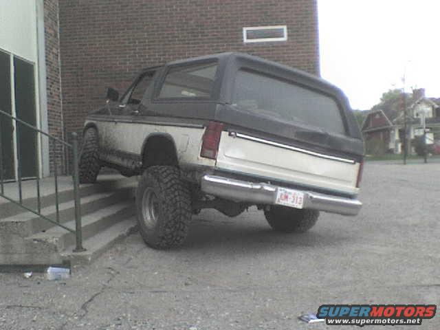 1985 Ford Bronco parked on a gravel lot next to a brick building, rear view