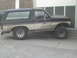 1985 Ford Bronco - A dirty, two-tone Ford Bronco with a camper shell is parked on a gravel surface.