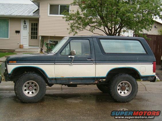 Side view of a dark blue and white Ford Bronco with aftermarket wheels parked on a street