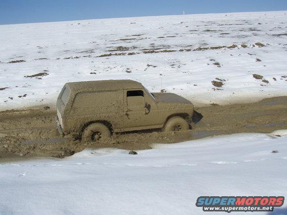 Mud-covered 1985 Ford Bronco stuck in mud with snow in background