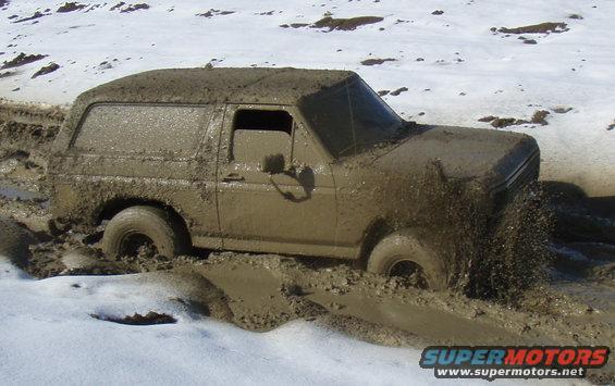 1985 Ford Bronco stuck deep in mud with snow on the ground