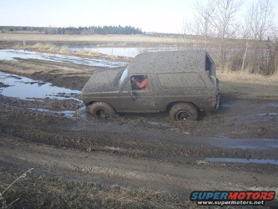 Muddy SUV stuck in a muddy field. Driver visible inside