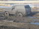 1985 Ford Bronco - A mud-covered SUV is stuck in a muddy field, with the driver visible inside.