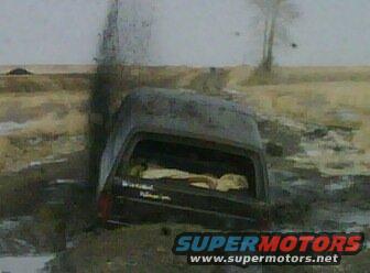 Dark SUV stuck in mud, emitting smoke from rear
