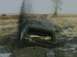 1985 Ford Bronco - A dark-colored SUV is deeply stuck in muddy terrain, with smoke billowing from its rear.
