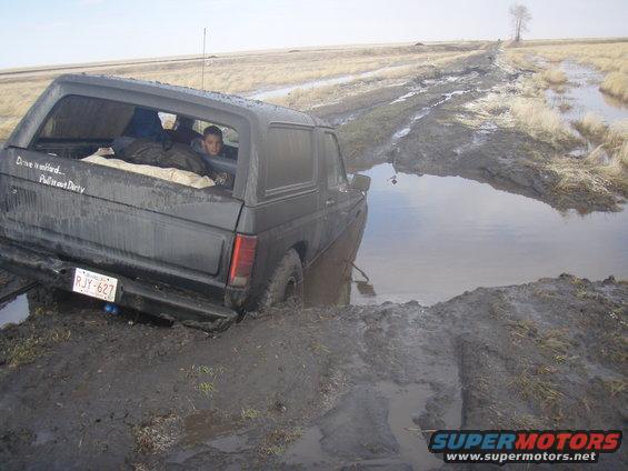 1985 Ford Bronco stuck in a muddy ditch with a person in the back window