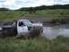 1985 Ford Bronco - A pickup truck navigates a muddy waterway, kicking up a large spray.