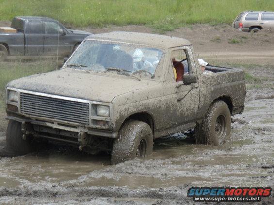 Muddy pickup truck stuck in mud pit, another truck and SUV visible in background
