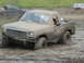1985 Ford Bronco - Muddy pickup truck struggling in a mud pit with other vehicles nearby.