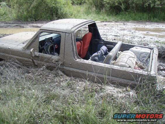 Ford Bronco stuck in mud, driver's side visible, red seats, cargo in bed