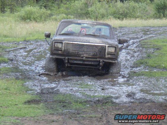 Mud-splattered SUV stuck in mud, front view. Grille and headlights visible