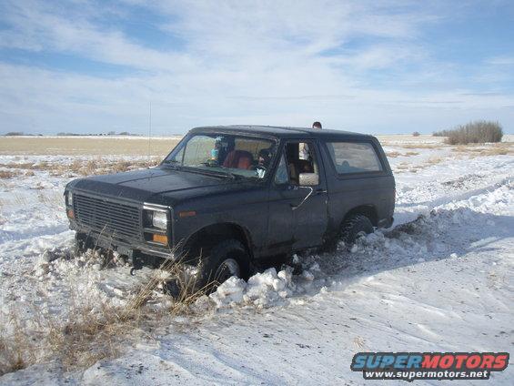 Dark colored Ford Bronco stuck in snowdrift, front wheels buried