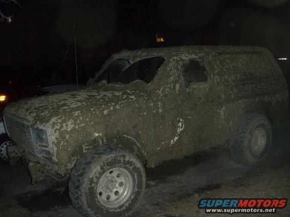 Mud-covered 1980s Ford Bronco, front quarter view, with cracked windshield and damaged front bumper